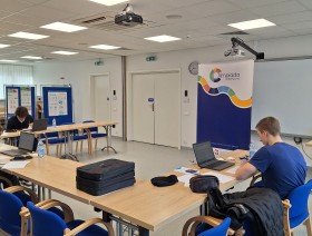 Uczniowie biorący udział w olimpiadzie siedzący przy stołach ustawionych w kształt litery U